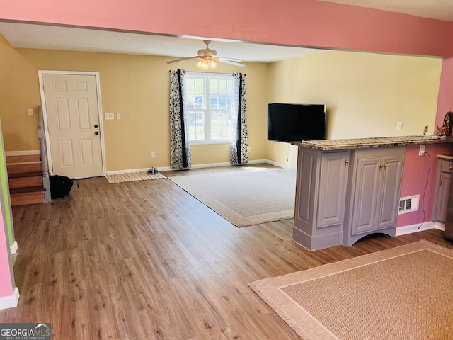 unfurnished living room featuring visible vents, a ceiling fan, light wood finished floors, baseboards, and stairs