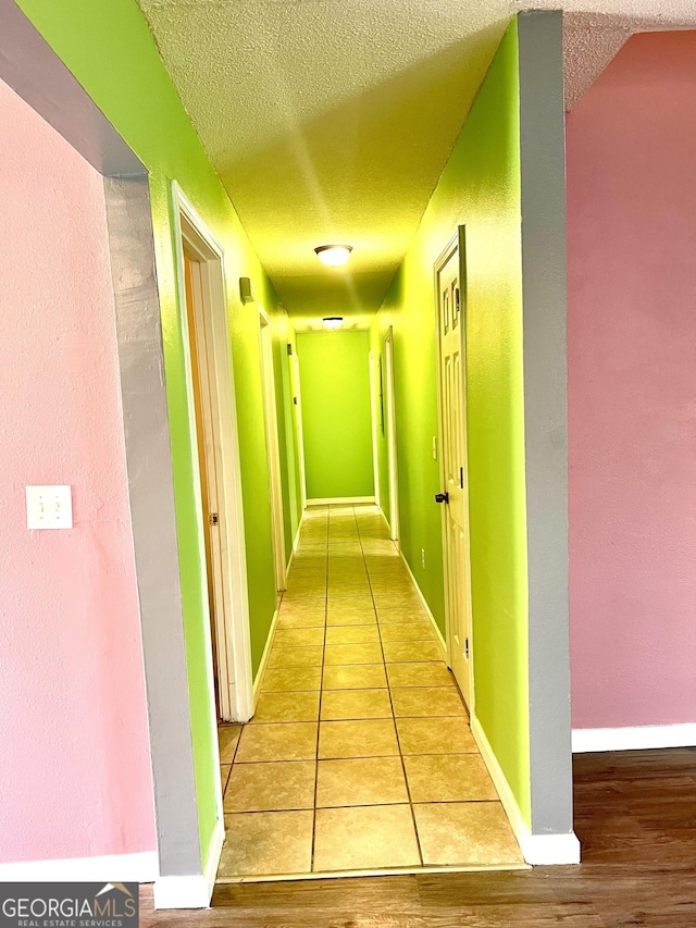 hallway featuring tile patterned floors, baseboards, and a textured ceiling