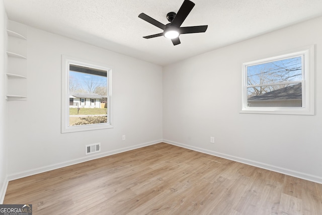 unfurnished room featuring light wood-style flooring, plenty of natural light, visible vents, and a textured ceiling