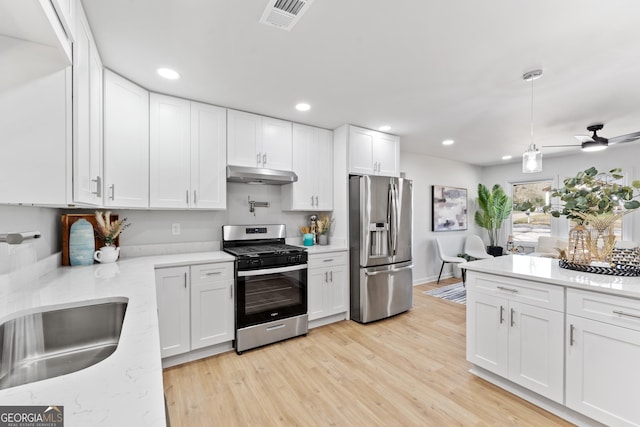 kitchen with a sink, under cabinet range hood, appliances with stainless steel finishes, white cabinetry, and light wood-type flooring