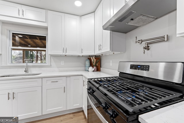 kitchen featuring stainless steel gas range oven, white cabinetry, under cabinet range hood, and a sink