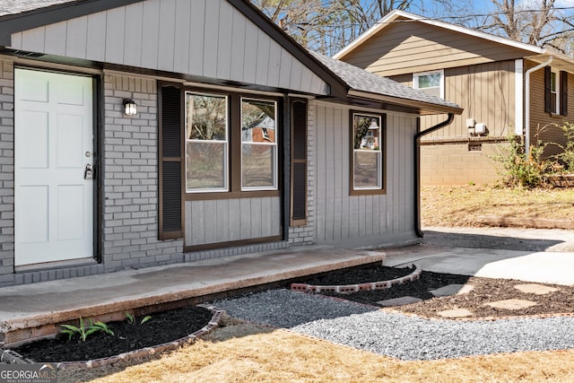 doorway to property with brick siding and roof with shingles