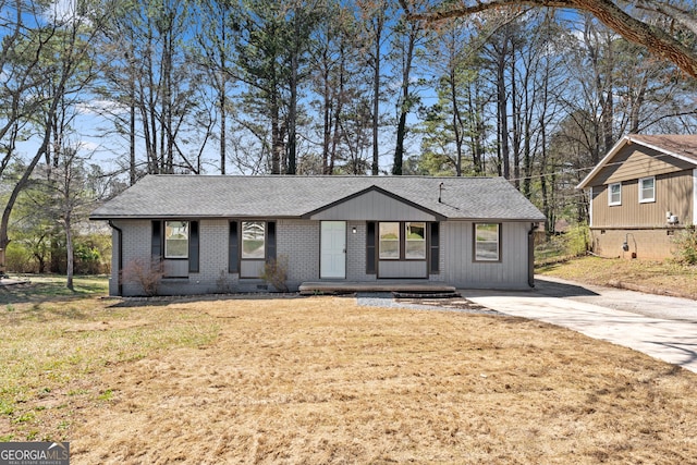 view of front of house with a front yard, concrete driveway, brick siding, and roof with shingles