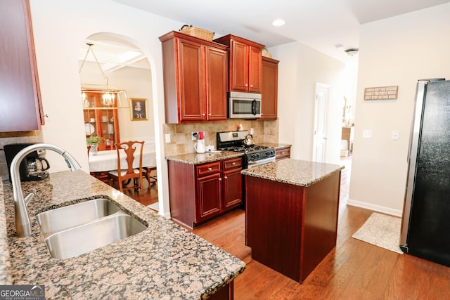 kitchen featuring a sink, decorative backsplash, wood finished floors, stainless steel appliances, and reddish brown cabinets