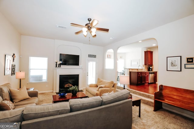 living room with visible vents, a fireplace, arched walkways, ceiling fan, and dark carpet