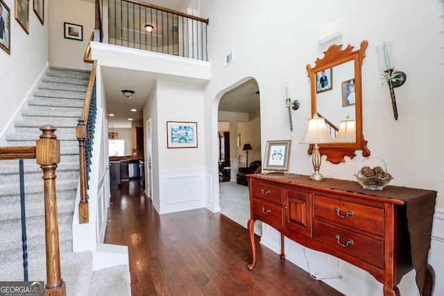 entryway with visible vents, arched walkways, a high ceiling, wainscoting, and dark wood-style flooring