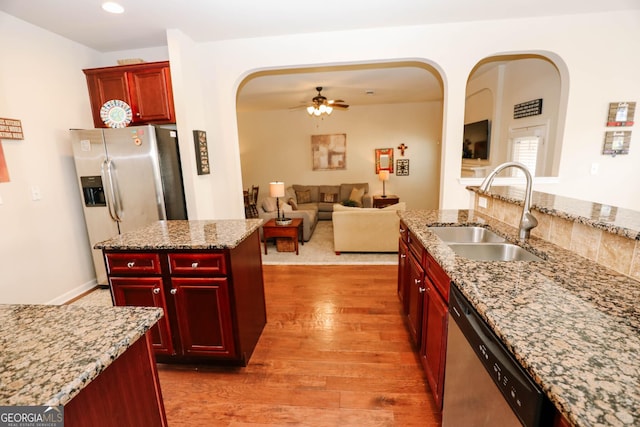 kitchen featuring dark brown cabinets, wood finished floors, arched walkways, stainless steel appliances, and a sink