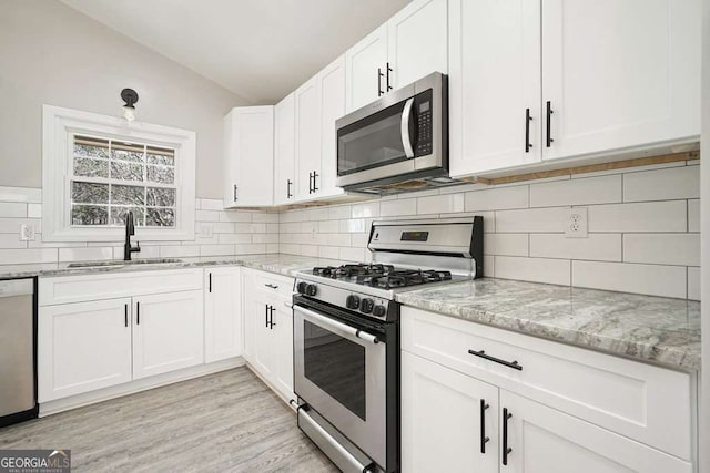 kitchen with a sink, white cabinetry, stainless steel appliances, lofted ceiling, and light stone countertops