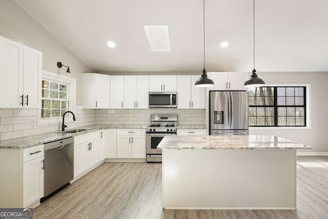 kitchen with a center island, light stone counters, stainless steel appliances, white cabinetry, and a sink