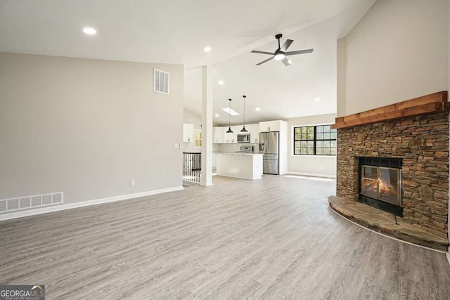 unfurnished living room with baseboards, visible vents, ceiling fan, a stone fireplace, and light wood-style floors