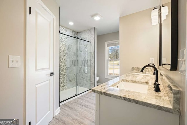 bathroom featuring double vanity, a stall shower, wood finished floors, and a sink