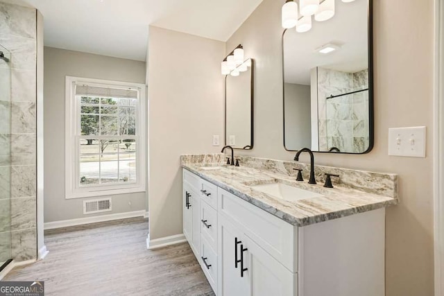 bathroom with wood finished floors, tiled shower, visible vents, and a sink