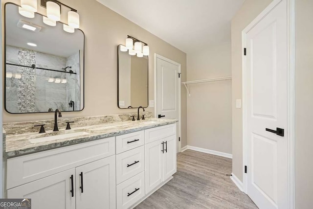 bathroom with a sink, wood finished floors, a stall shower, and double vanity