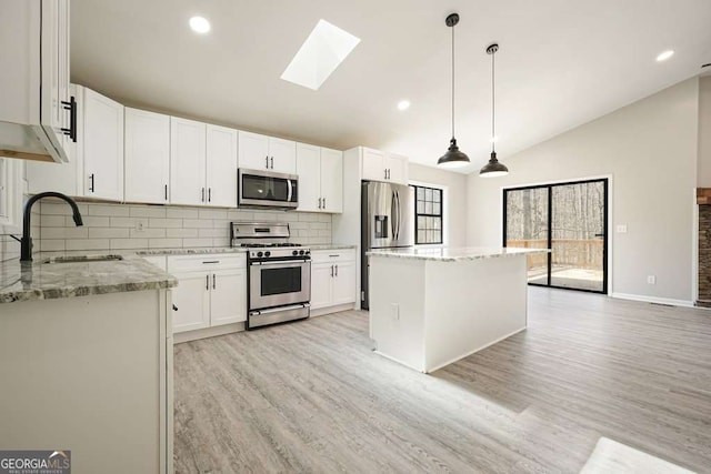 kitchen featuring a kitchen island, lofted ceiling with skylight, light stone counters, stainless steel appliances, and a sink