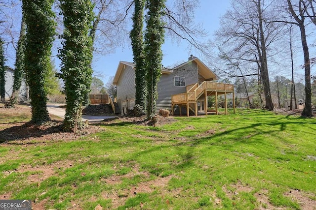 rear view of house with stairway, driveway, a wooden deck, an attached garage, and a lawn