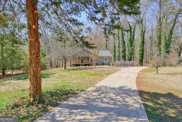 view of front of house featuring a view of trees, a front yard, driveway, and fence