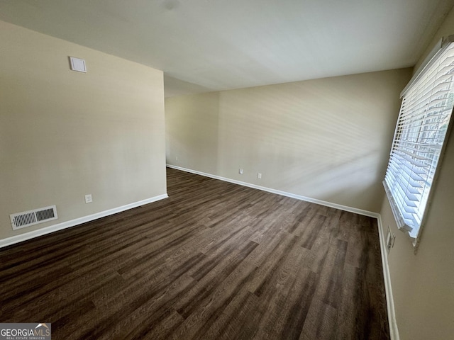 spare room with visible vents, baseboards, and dark wood-type flooring