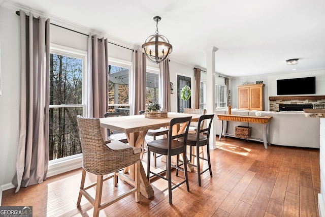 dining space featuring a notable chandelier, a stone fireplace, light wood-style flooring, and ornamental molding