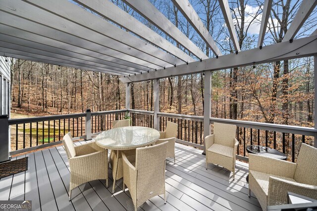 wooden deck with a view of trees and outdoor dining space