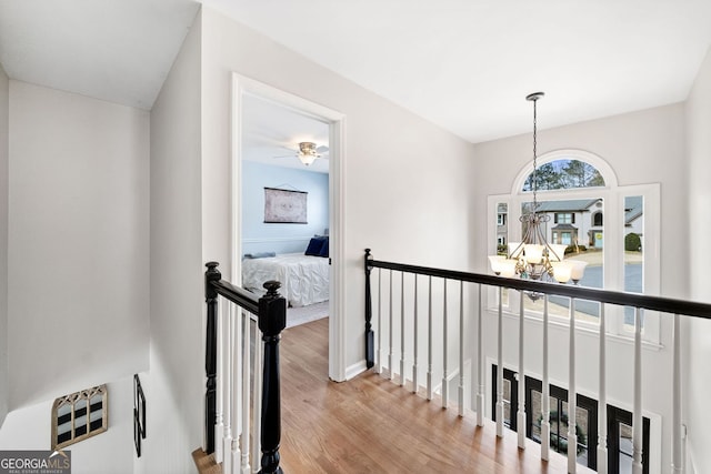 corridor featuring an upstairs landing, a notable chandelier, and wood finished floors