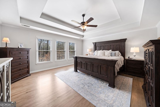 bedroom featuring baseboards, a raised ceiling, and light wood finished floors