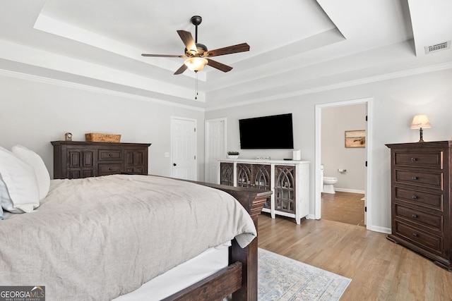 bedroom featuring visible vents, baseboards, light wood-type flooring, and a tray ceiling