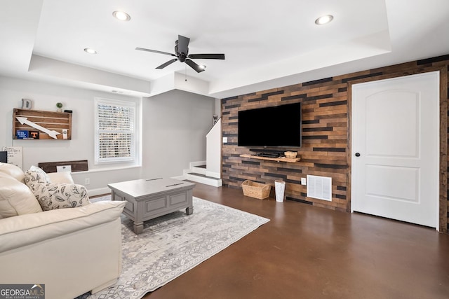 living room featuring finished concrete floors, recessed lighting, a raised ceiling, and an accent wall