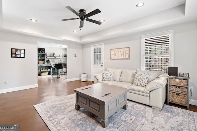 living room featuring a raised ceiling, recessed lighting, and baseboards