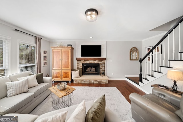 living area featuring crown molding, baseboards, stairs, a stone fireplace, and dark wood-style floors