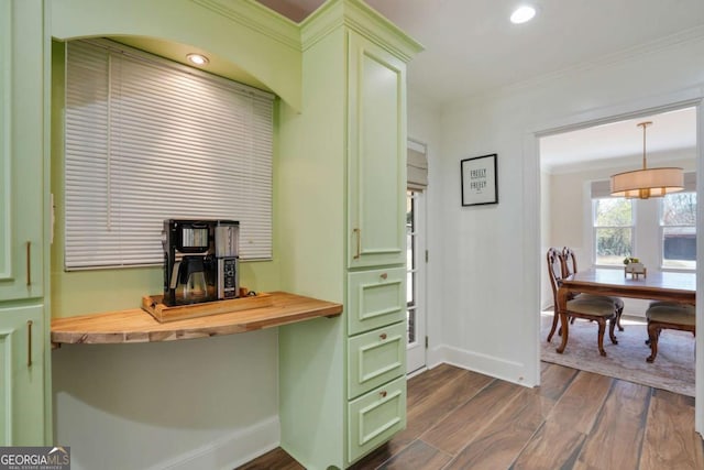 interior space featuring dark wood-style floors, baseboards, ornamental molding, butcher block countertops, and green cabinets