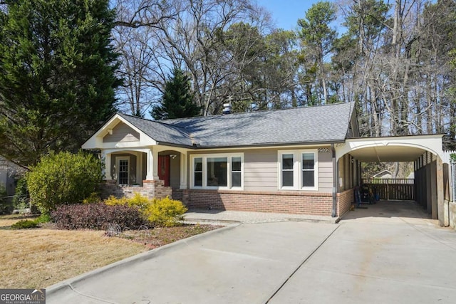 view of front of property featuring brick siding, an attached carport, fence, concrete driveway, and roof with shingles