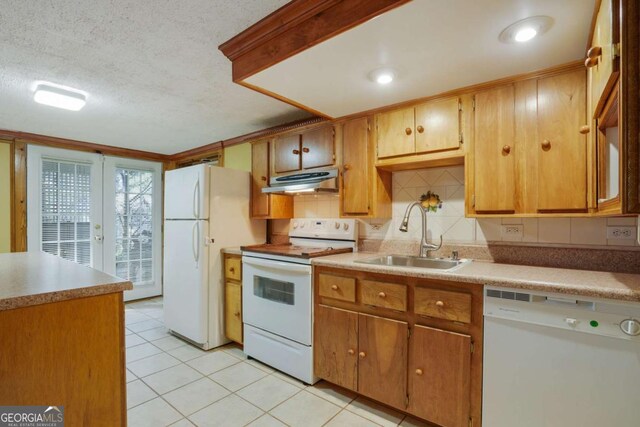 kitchen with a sink, under cabinet range hood, white appliances, light tile patterned flooring, and decorative backsplash