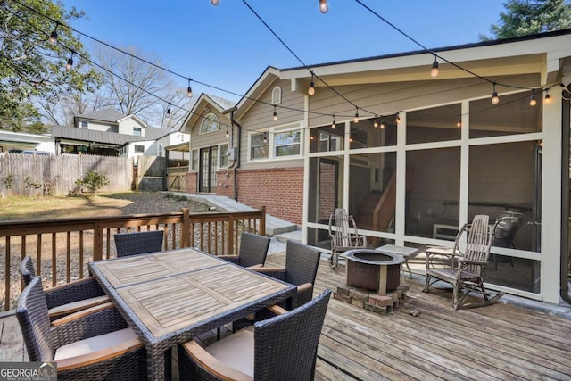 wooden terrace with a sunroom, a fire pit, outdoor dining space, and fence