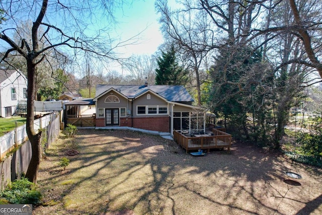 view of front of house with brick siding, fence, french doors, a deck, and a sunroom