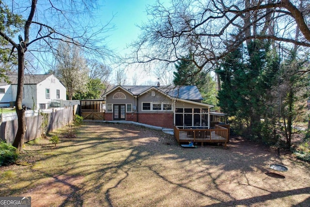 view of front of home with brick siding, fence, french doors, a deck, and a sunroom