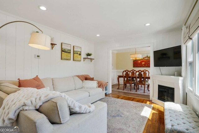 living room with crown molding, a decorative wall, recessed lighting, and wood finished floors