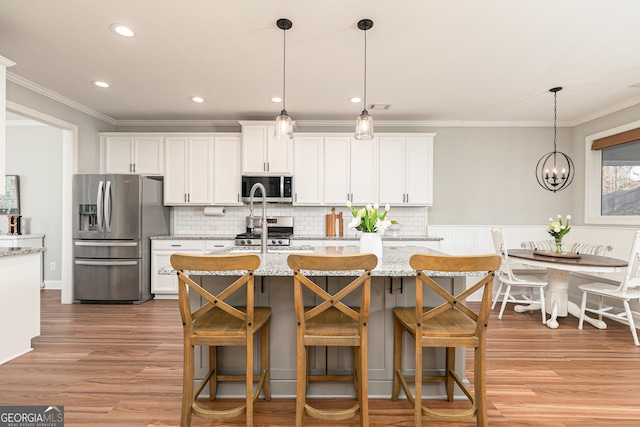 kitchen with an island with sink, light wood-style floors, appliances with stainless steel finishes, white cabinetry, and crown molding