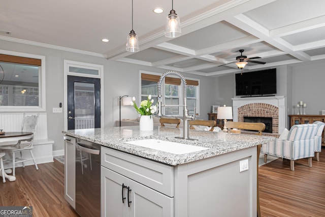 kitchen with a sink, decorative light fixtures, stainless steel dishwasher, a fireplace, and dark wood-style flooring