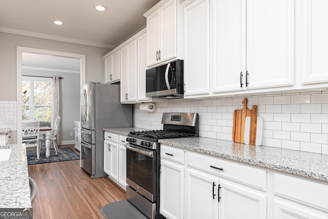 kitchen featuring light wood-type flooring, tasteful backsplash, appliances with stainless steel finishes, white cabinets, and crown molding