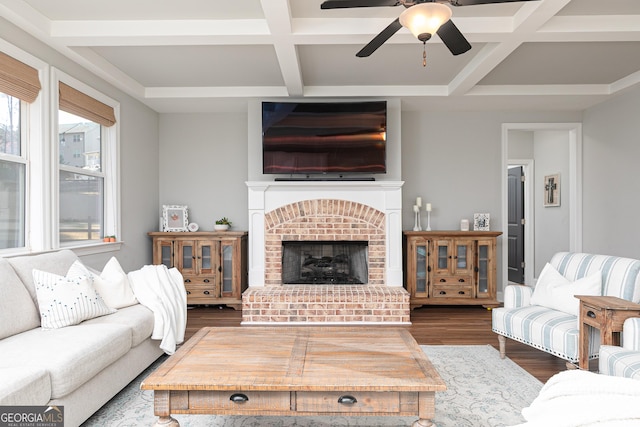 living area featuring beam ceiling, a brick fireplace, wood finished floors, and coffered ceiling