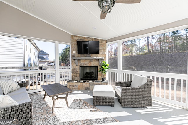 sunroom / solarium with an outdoor stone fireplace, ceiling fan, and vaulted ceiling