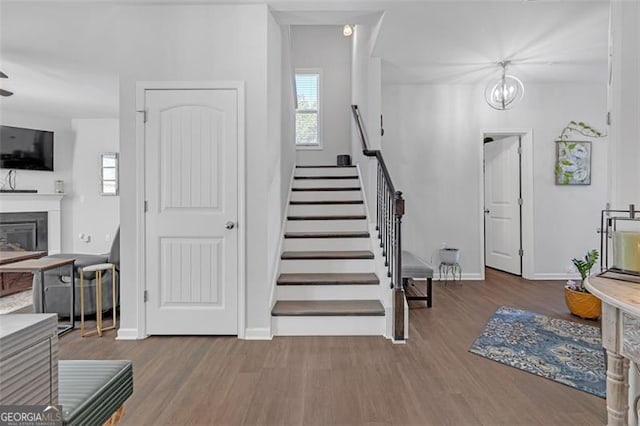 staircase with a glass covered fireplace, an inviting chandelier, baseboards, and wood finished floors