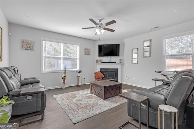 living room featuring visible vents, baseboards, ceiling fan, wood finished floors, and a glass covered fireplace