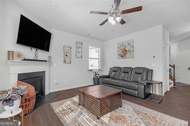 living room featuring a glass covered fireplace, ceiling fan, baseboards, and wood finished floors