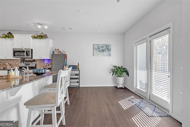 kitchen featuring stainless steel microwave, dark wood-type flooring, stone counters, a kitchen breakfast bar, and white cabinets