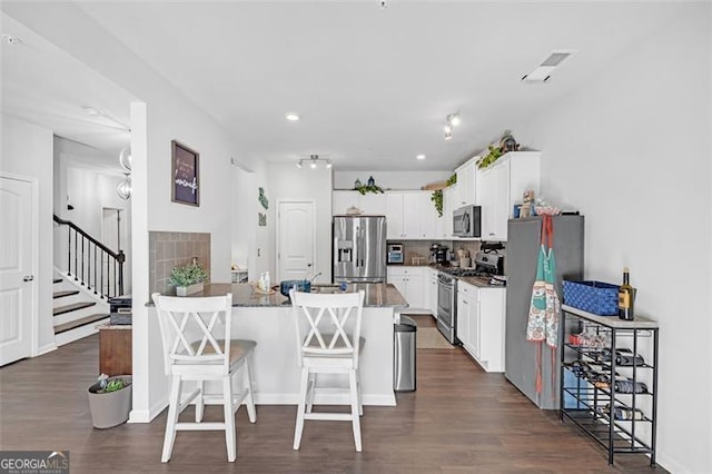 kitchen featuring a breakfast bar, dark wood finished floors, appliances with stainless steel finishes, a peninsula, and white cabinets