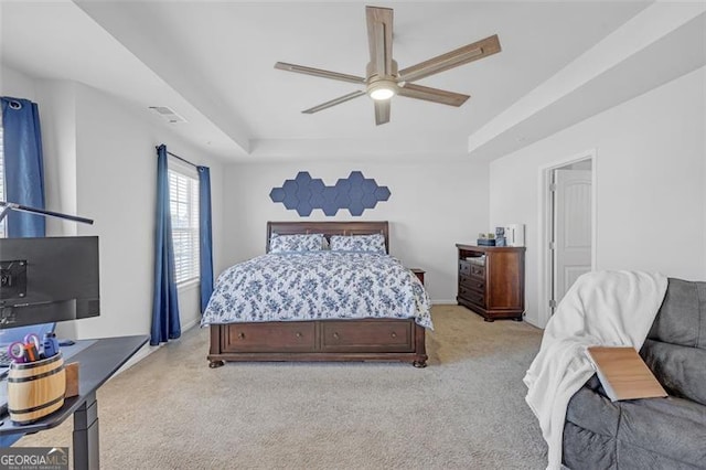 bedroom with visible vents, light colored carpet, a ceiling fan, and a tray ceiling