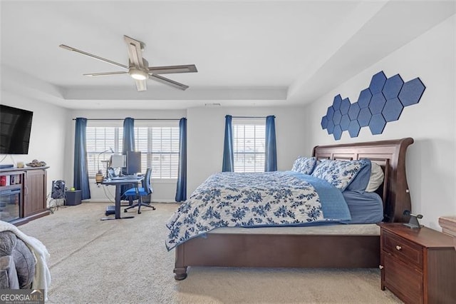 carpeted bedroom featuring a tray ceiling, multiple windows, and ceiling fan