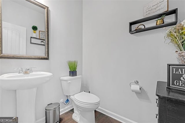 bathroom featuring toilet, wood finished floors, baseboards, and a sink