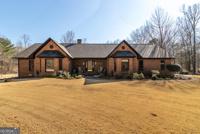 view of front of property with brick siding, a chimney, a front yard, and roof with shingles